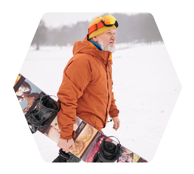 An elderly man walks in a winter jacket and holds a snowboard