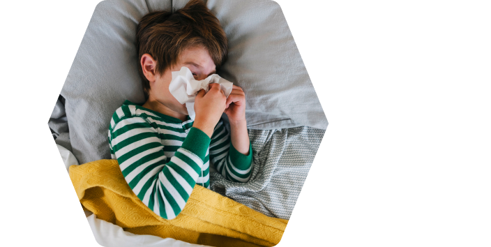 A sick boy lies in bed and blows his nose in a tissue